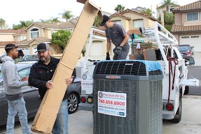 Two technicians are loading a large air conditioning unit onto a truck